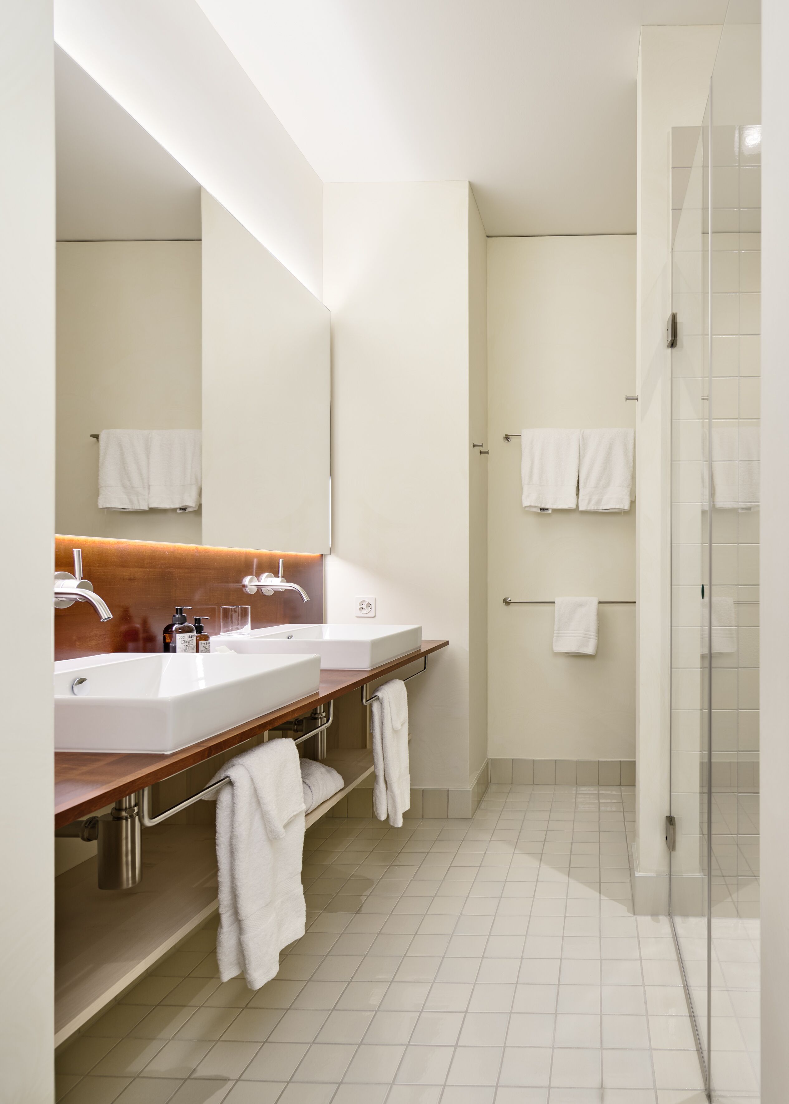 Un baño moderno con dos lavamanos, una ducha y una zona de ducha con mampara de vidrio.