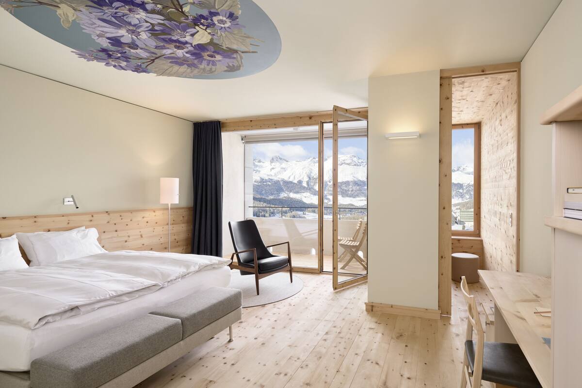Une chambre d’hôtel avec un lit, une chaise, un bureau et une vue sur les montagnes.