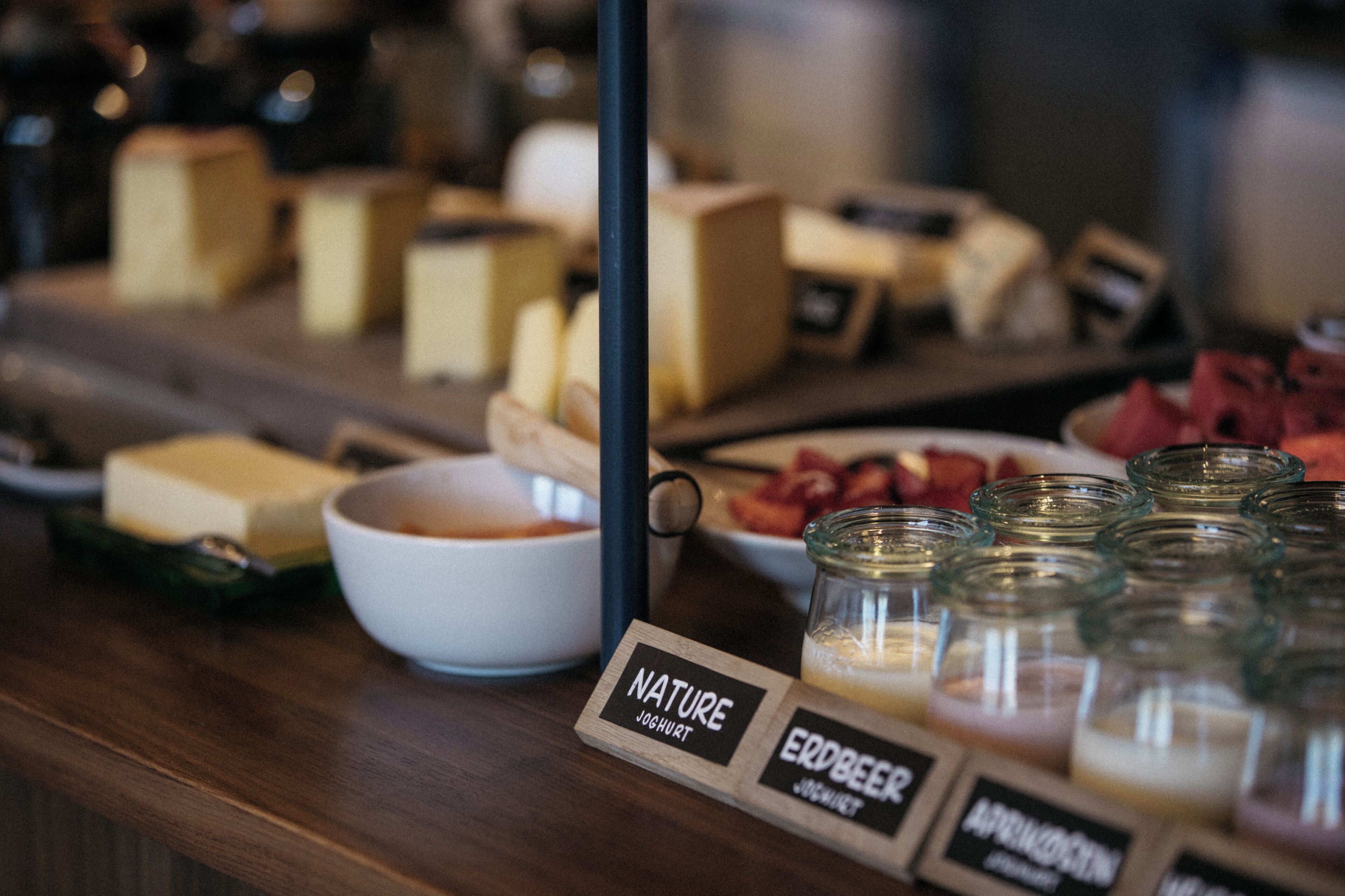 A selection of cheeses and yogurt on a wooden counter with labels indicating 'Nature Yogurt' and 'Erdbier Yogurt'.
