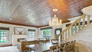 A spacious dining area with a large wooden table and chairs, a chandelier, and a staircase with wooden railings. - Above Escape LT I Lake Travis I Pool&Spa I Services I Pets (Austin)