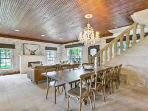 Un comedor amplio con una gran mesa de madera y sillas, una araña y una escalera con barandilla de madera.