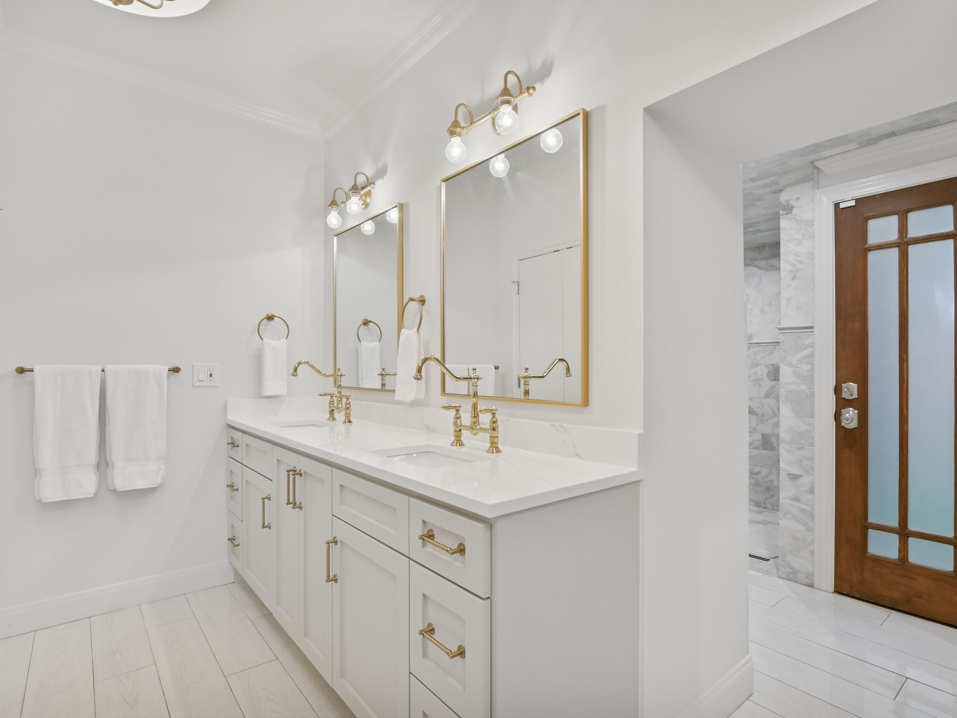 A modern bathroom with two sinks, gold fixtures, and large mirrors.