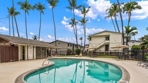 A swimming pool surrounded by palm trees and a building with a balcony.