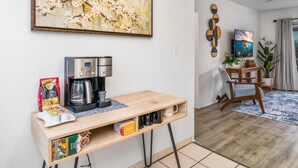 A compact living space with a coffee station, a painting, and a dining area.