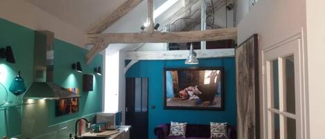 A kitchen with wooden beams, a sink, and a dining area with a purple sofa and a red rug.