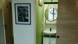 Een slaapkamer met een bed, een nachtkastje met een handdoek, een spiegel, een wastafel en een lijst met een afbeelding aan de muur.