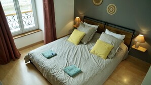 Een net opgemaakt bed met een grijs-wit geruit sprei, twee kussens en twee bedlampjes.
