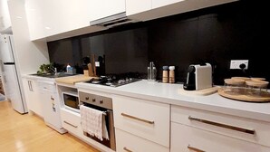 A modern kitchen with white cabinetry, a black backsplash, stainless steel appliances, and wooden flooring. - Stunning Family Retreat Perfect Location (melbourne)