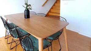 A dining area with a wooden table and black wire chairs, a vase with flowers, and a staircase in the background. - Stunning Family Retreat Perfect Location (melbourne)