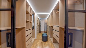 A narrow walk-through closet with wooden shelving and drawers, a central bench, and a ceiling light.
