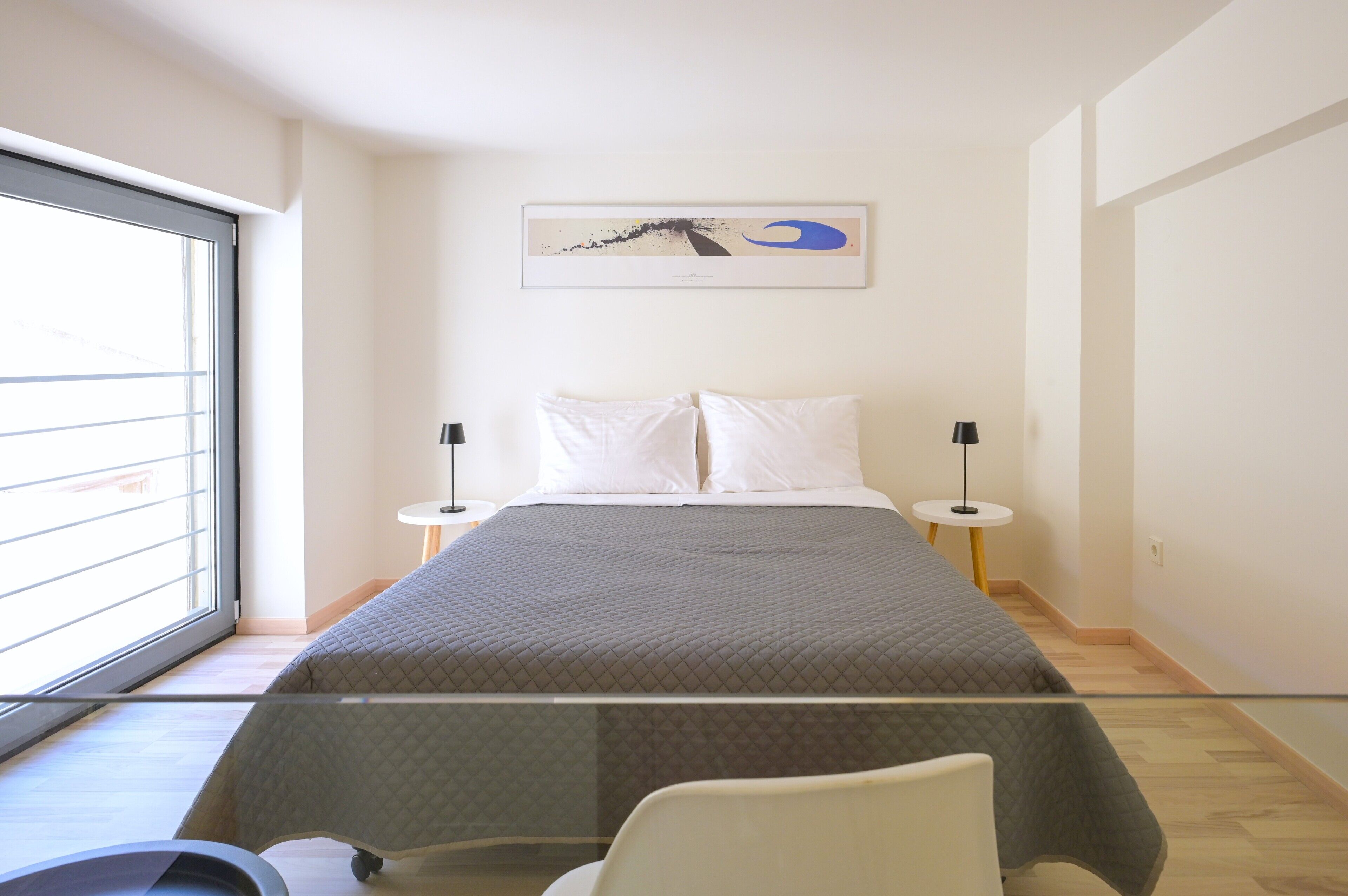Een moderne slaapkamer met een groot bed, twee nachtkastjes, een raam met zonwering en een kunstwerk aan de muur.