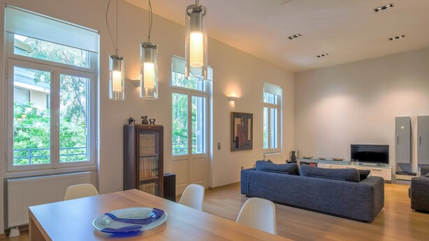 A modern living room with a wooden dining table, a gray sofa, and a TV.