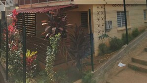 Un immeuble résidentiel à plusieurs étages, doté d’un balcon au deuxième étage, de climatiseurs et d’une entrée sécurisée par un portail.