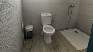 Une petite salle de bain carrelée, équipée de toilettes, d’un bidet et d’un espace douche.