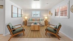 Ein Wohnzimmer mit einer Couch, zwei Sesseln, einem Couchtisch und einem Fenster mit Jalousien.