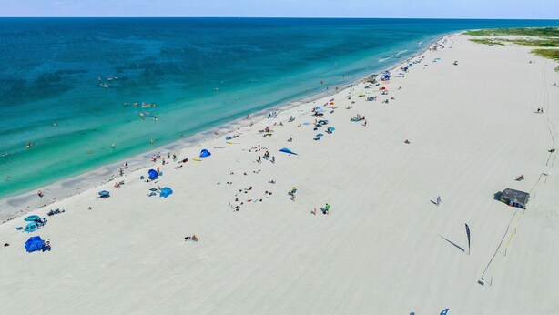 Ein Strand mit klarem türkisblauem Wasser und weißem Sand, sowie einigen Sonnenschirmen.