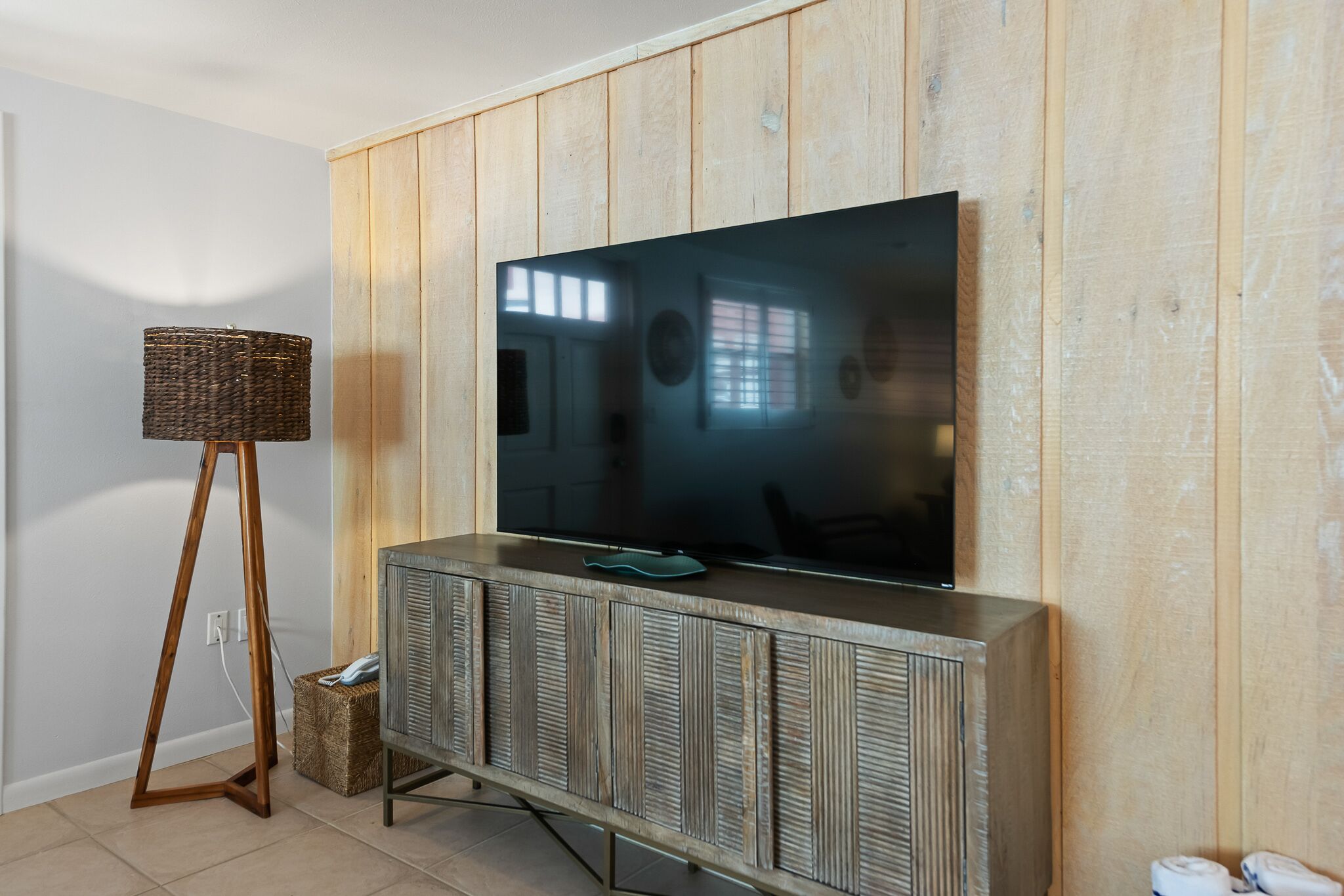 Een moderne woonkamer met een grote flatscreen televisie bevestigd aan een houten paneelwand, een vloerlamp en een houten kast met inbouwkasten.