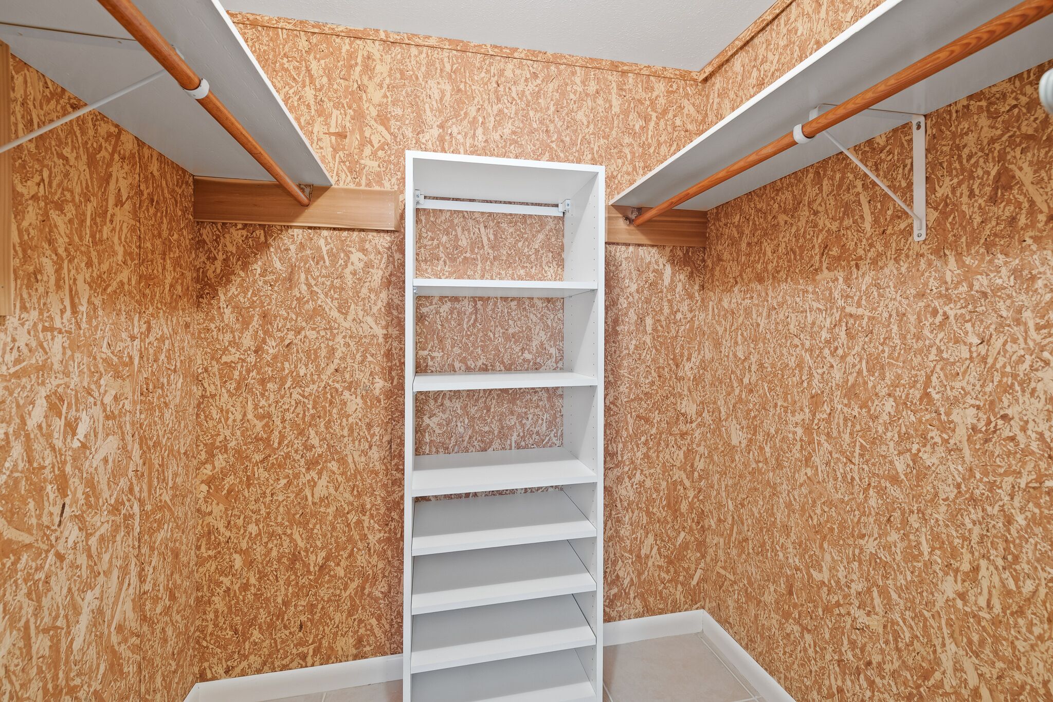 A room with a white shelving unit against a wooden wall, with a ceiling fan and wooden beams.
