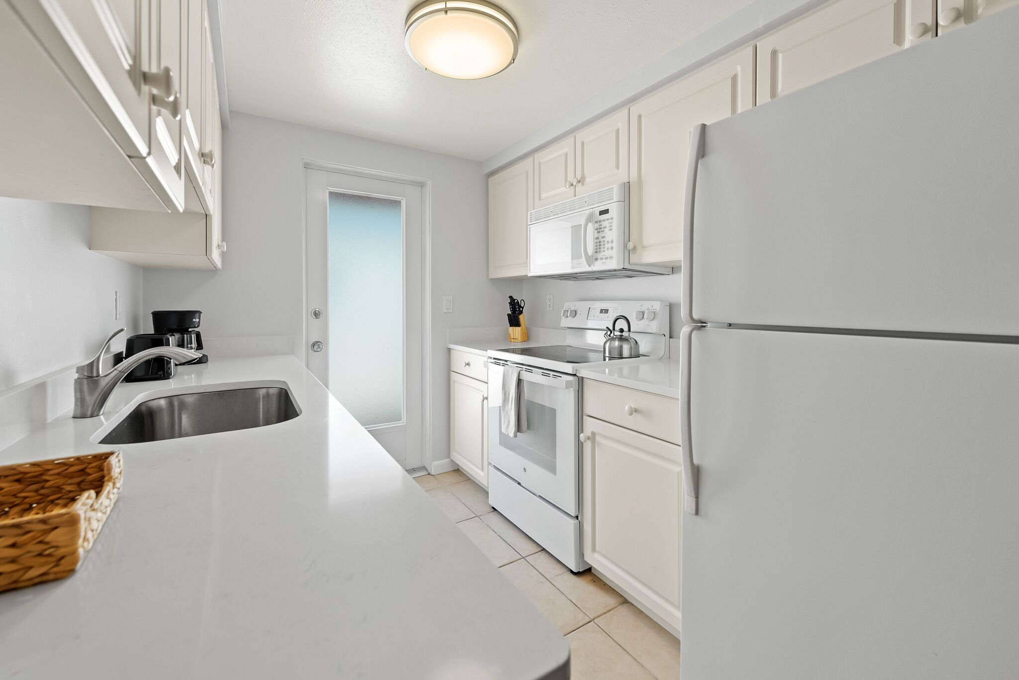 A modern kitchen with white cabinetry, a stainless steel sink, a microwave, and a refrigerator.