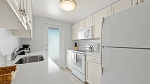 Eine moderne Küche mit weißen Schränken, einer Edelstahl-Spüle, einer Mikrowelle und einem Kühlschrank.