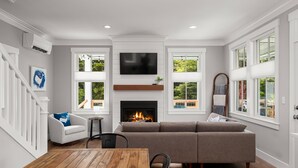 A modern living room with a fireplace, a television, and a dining area. - Seabrook White Whale | Hot Tub, Workspace, 3BR | Sleeps 8, South Farm (Pacific Beach)
