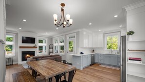 A spacious kitchen with white cabinets, a wooden dining table, and a built-in fireplace. - Seabrook White Whale | Hot Tub, Workspace, 3BR | Sleeps 8, South Farm (Pacific Beach)