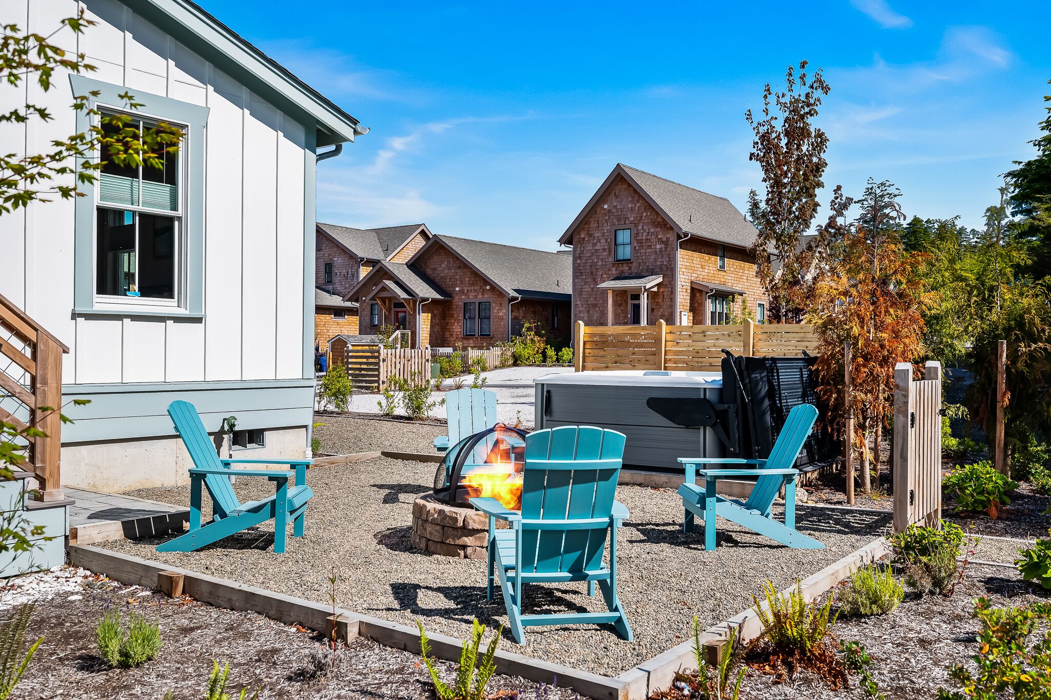 A backyard with a fire pit, two Adirondack chairs, and a wooden deck.