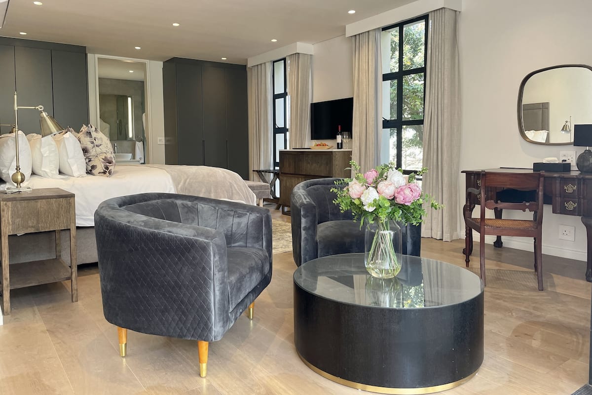 Une chambre d’hôtel moderne avec un grand lit, une table basse ronde noire, deux fauteuils, un bureau et un téléviseur.