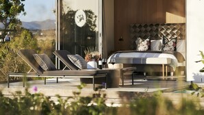 Un dormitorio moderno con una cama grande, dos sillones, una mesita con copas de vino y vistas al exterior.