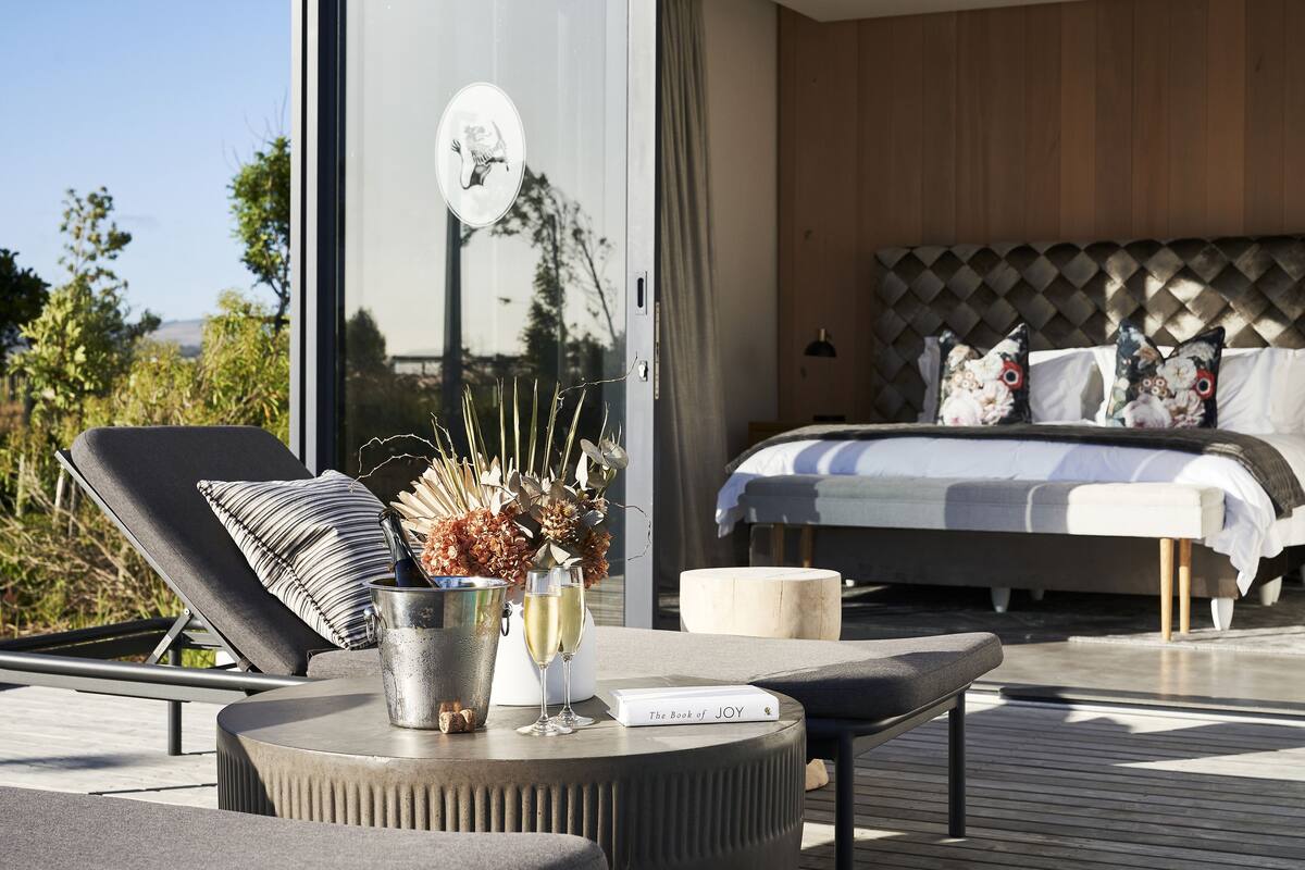 Une chambre à coucher moderne avec un grand lit, une table de chevet sur laquelle repose un livre, et une vue sur l’extérieur.