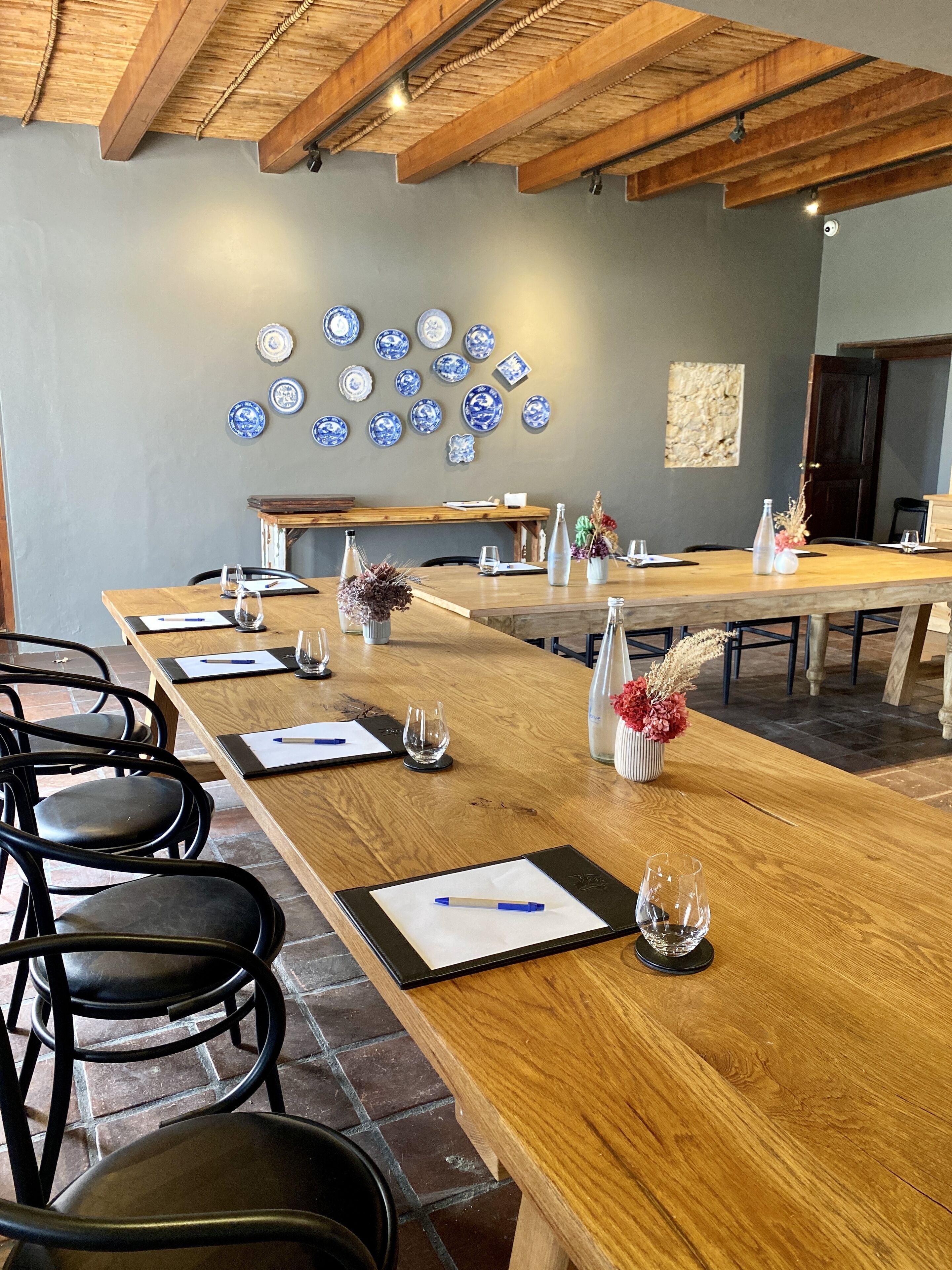 A conference room with a long wooden table, black chairs, and a wall decorated with blue and white plates.
