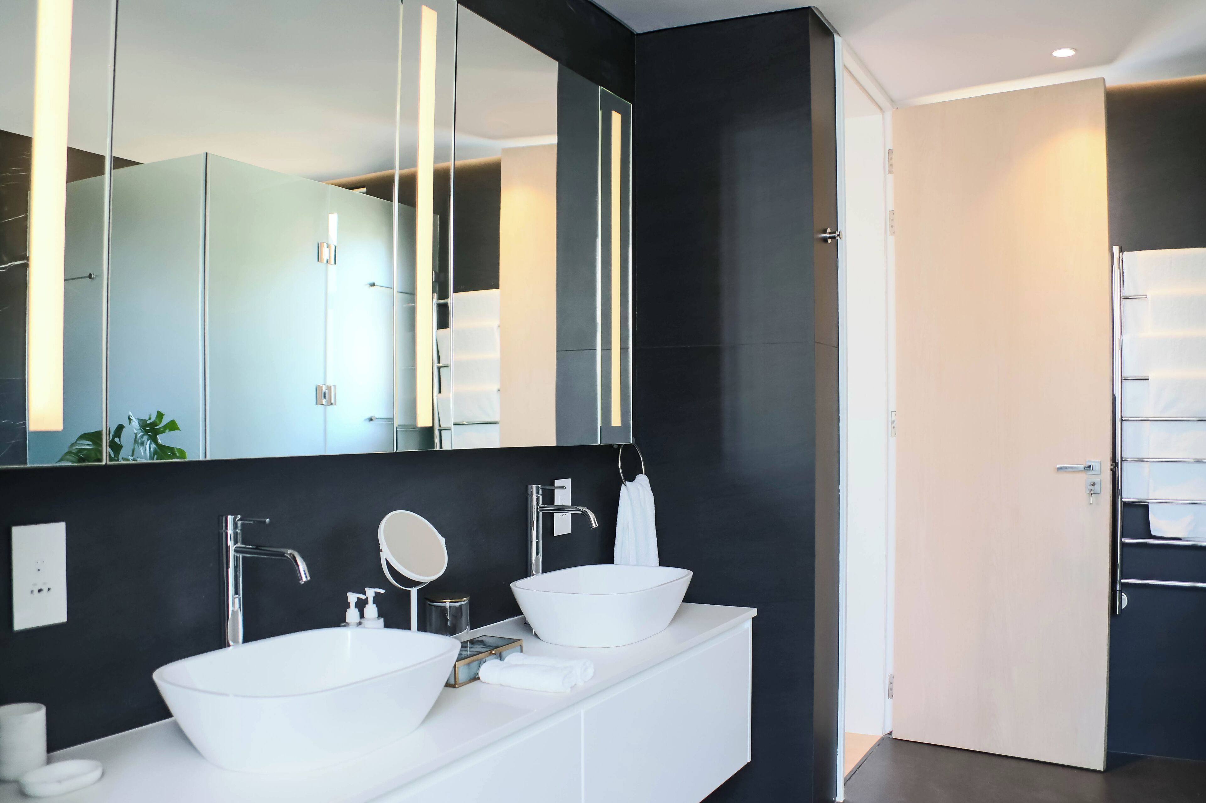 Une salle de bain moderne avec un grand miroir, deux lavabos et un porte-serviettes.