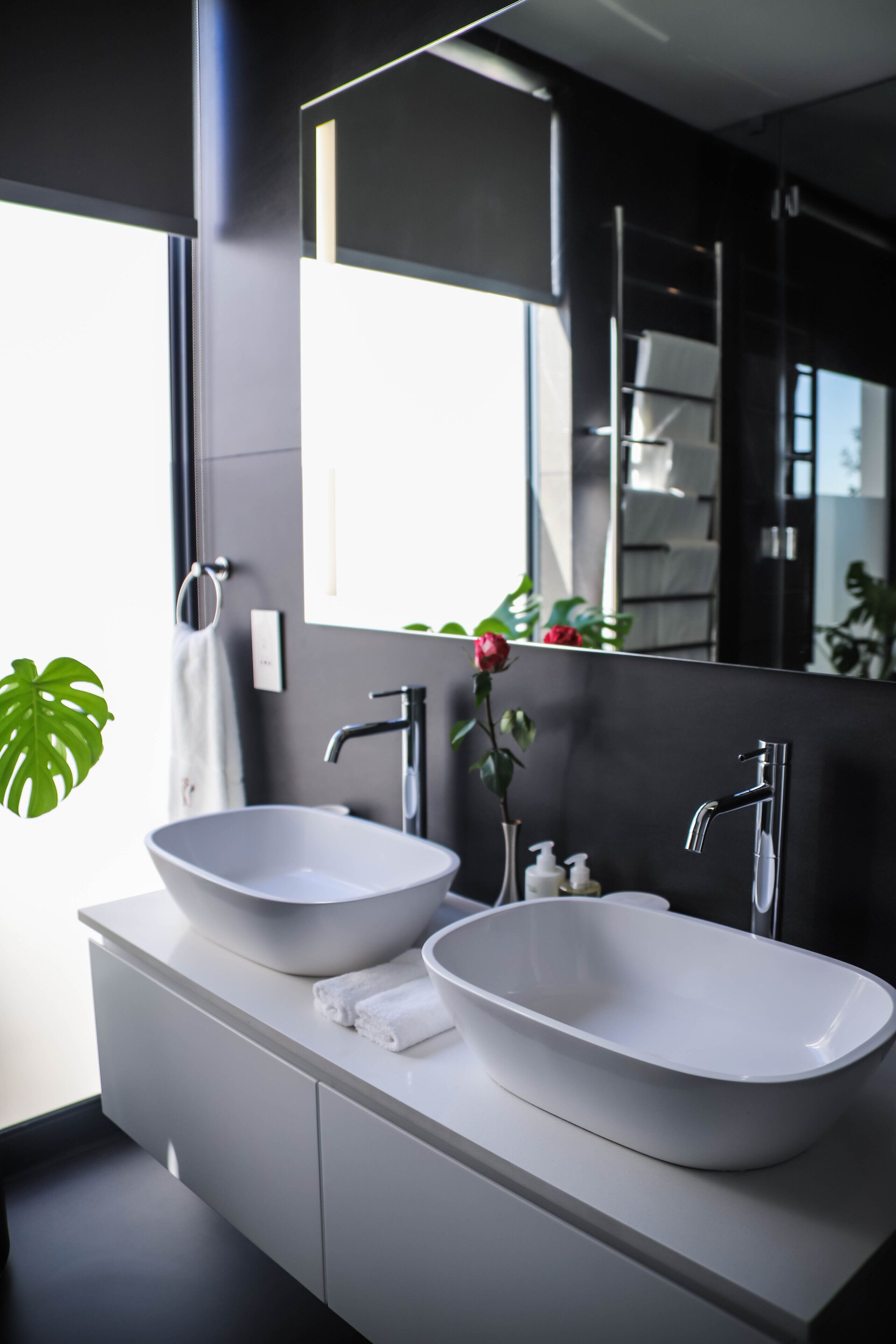 Un baño moderno con dos lavamanos tipo recipiente blancos, un espejo grande y una planta en maceta.