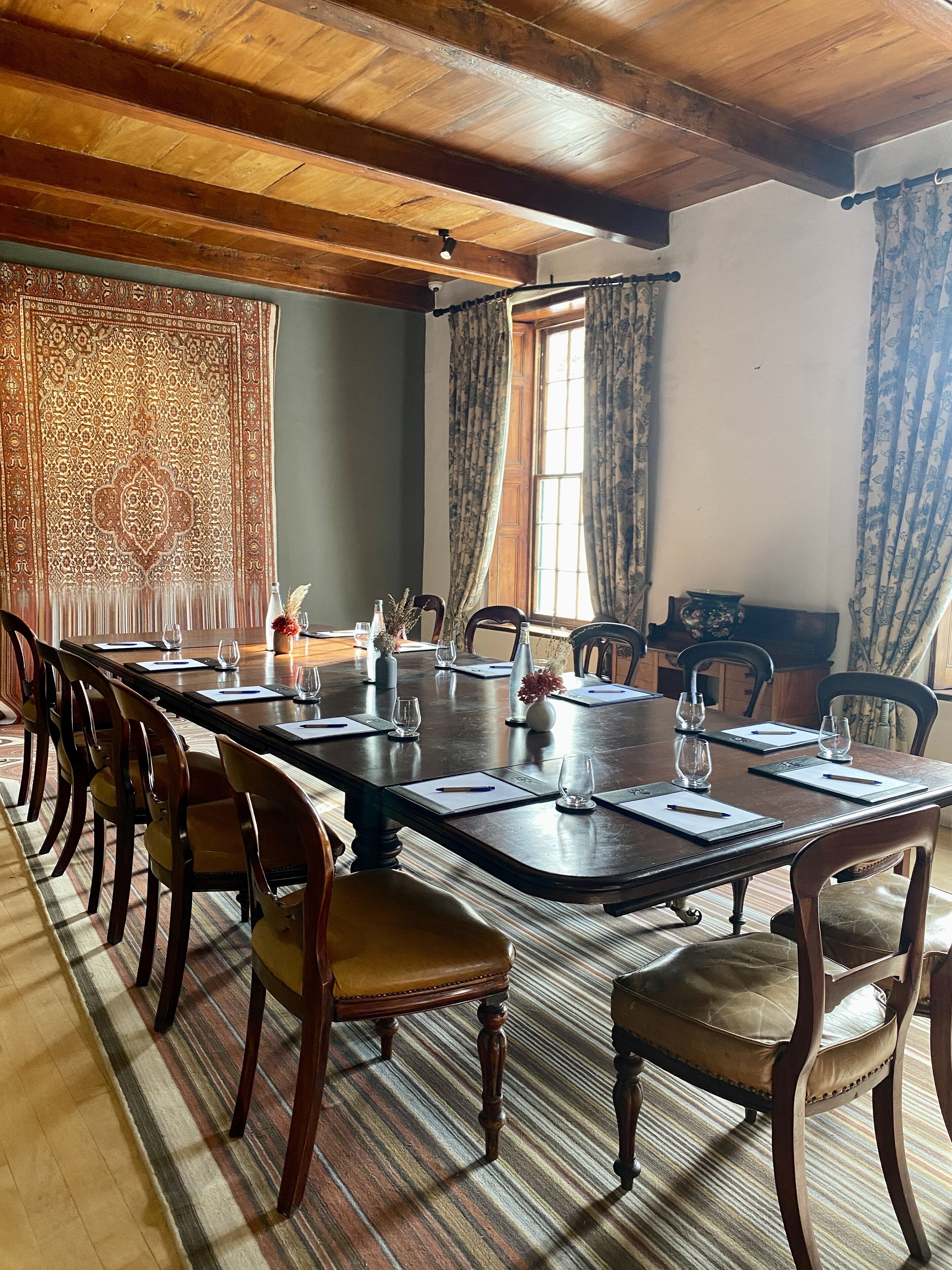 Un salón de conferencias con una mesa larga, sillas y un tapiz decorativo en la pared.