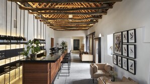 Zona de bar moderna con mostrador de madera, taburetes y un área de estar con sofá y sillas.