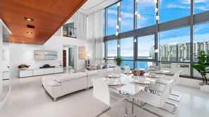 Un salón moderno y espacioso con un comedor grande listo para seis comensales, un sofá blanco y una cocina con un letrero que dice "LUXURY RENTALS Miami Beach".