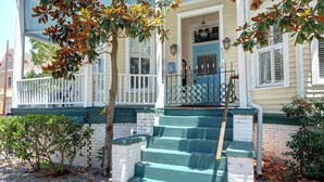 Une maison à deux étages avec une porte bleue, des volets blancs et une balustrade verte sur le porche.