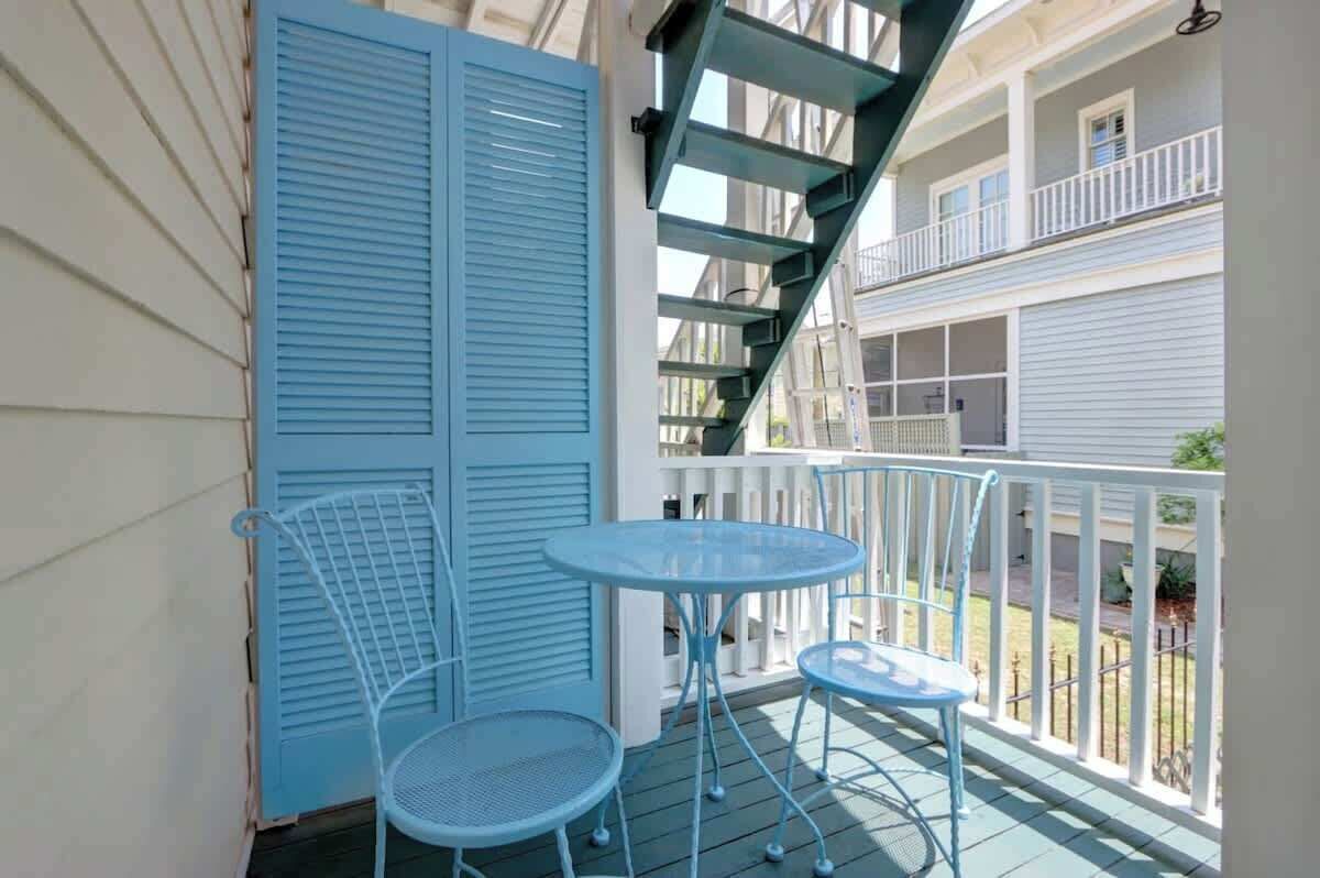 A balcony with a blue metal table and chairs, a white railing, and a view of a neighboring building.