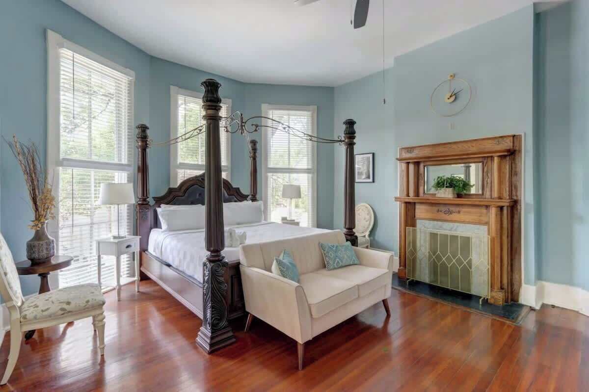 Une chambre à coucher avec un lit à baldaquin, une cheminée et une grande fenêtre équipée de stores.
