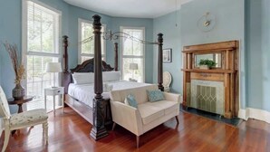 Une chambre à coucher avec un lit à baldaquin, une cheminée et une grande fenêtre équipée de stores.