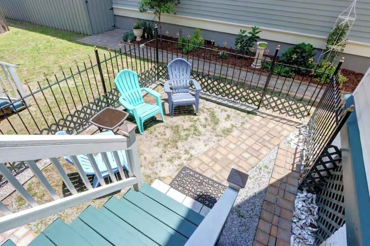 Un patio trasero con terraza de madera, dos sillas Adirondack y una mesita.