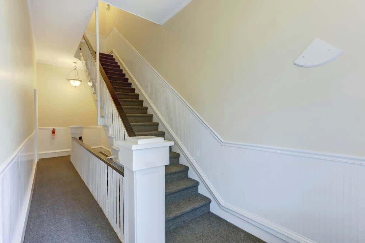 Eine Treppe mit weißen Geländern und Teppichboden, die zu einer Empore führt.