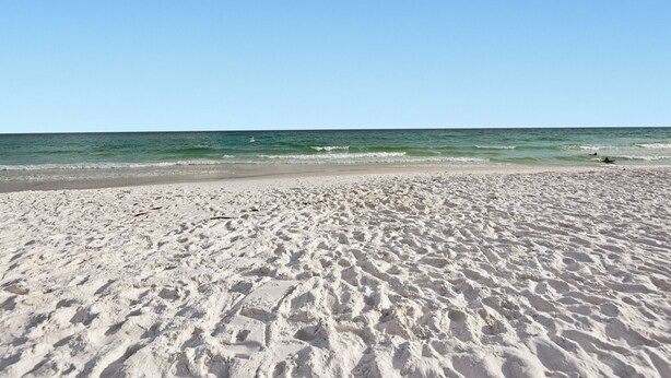Een zandstrand met rustige golven en een heldere lucht.
