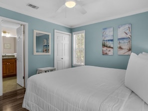 A bedroom with a large bed, a ceiling fan, and artwork on the walls.