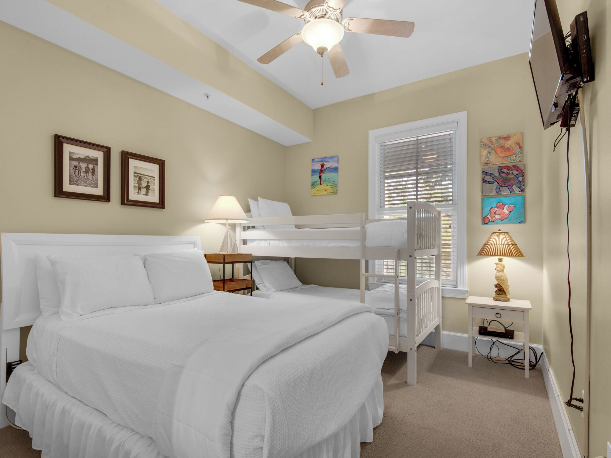A hotel room with a large bed, a smaller bed, a ceiling fan, a desk with a lamp, and artwork on the walls.