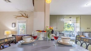 A dining area with a long table set for two, a vase with flowers, and a bottle of wine.