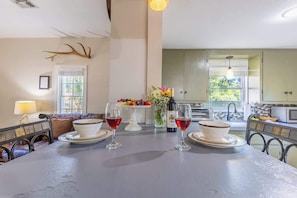 Un comedor con una mesa preparada para dos personas, un florero con flores y una cocina al fondo.