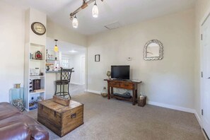 A living room with a brown leather couch, a wooden coffee table, a television on a wooden stand, and a decorative mirror on the wall.