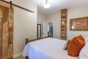 Une chambre à coucher avec un lit, une tête de lit en bois, une porte, un tableau accroché au mur et un luminaire au plafond.