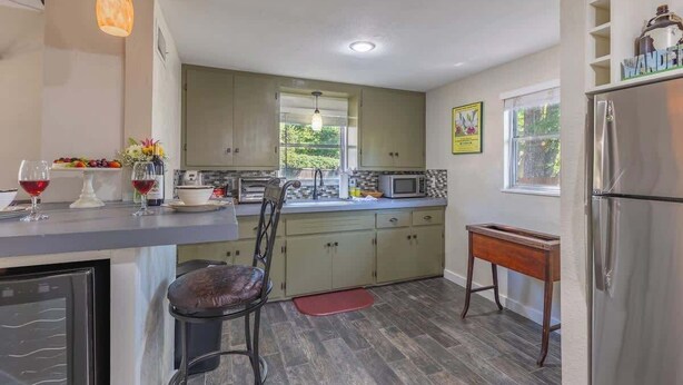 A modern kitchen with a built-in oven, microwave, and stainless steel refrigerator. There is a dining area with a chair and a small table.